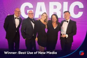 Five people in formal wear smile on stage with an award; text reads Winner: Best Use of New Media.