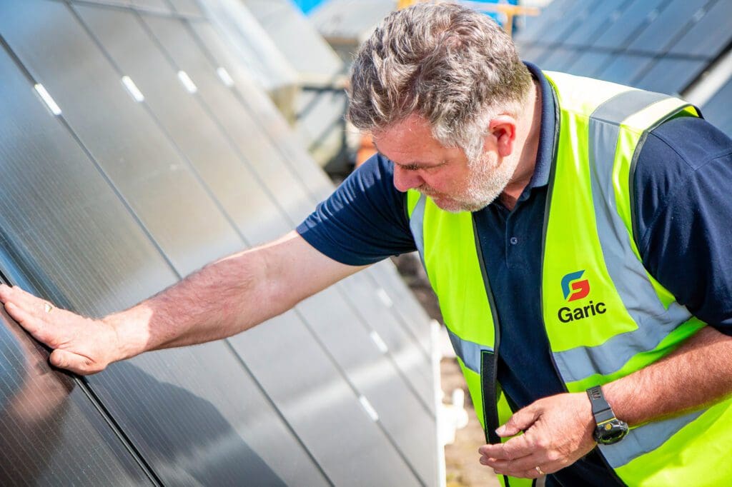 Man in a Garic vest inspects solar panels outdoors on a sunny day.