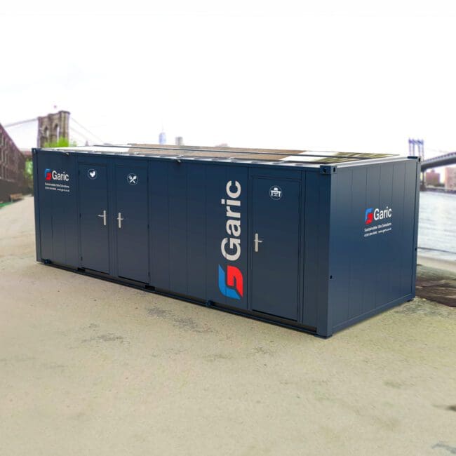 Eco Cabin 24 portable unit with doors, set outdoors near a river and a partially visible bridge.