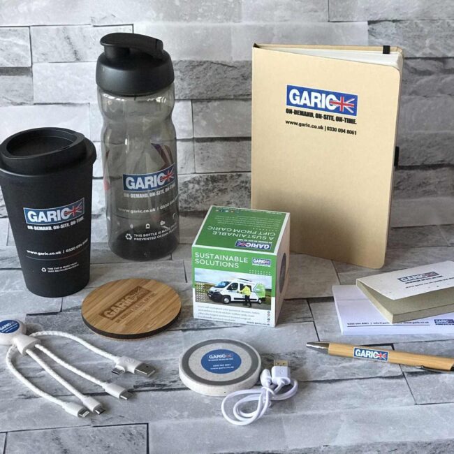 Assorted branded office supplies and drinkware with Garic UK logos arranged on a gray tiled surface.