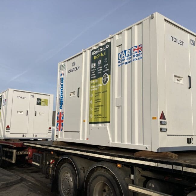 Two white portable container units labeled CANTEEN and TOILET on a flatbed truck.