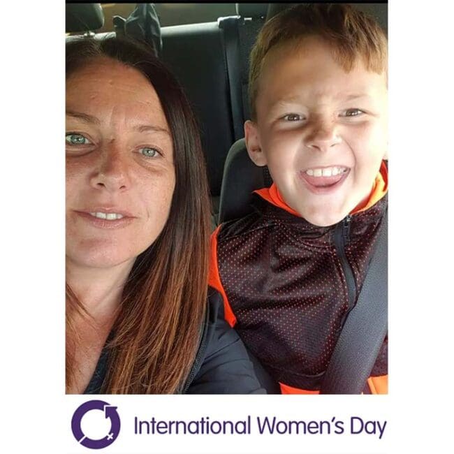 A woman and a smiling boy sit in a car. International Women’s Day logo and text appear below.
