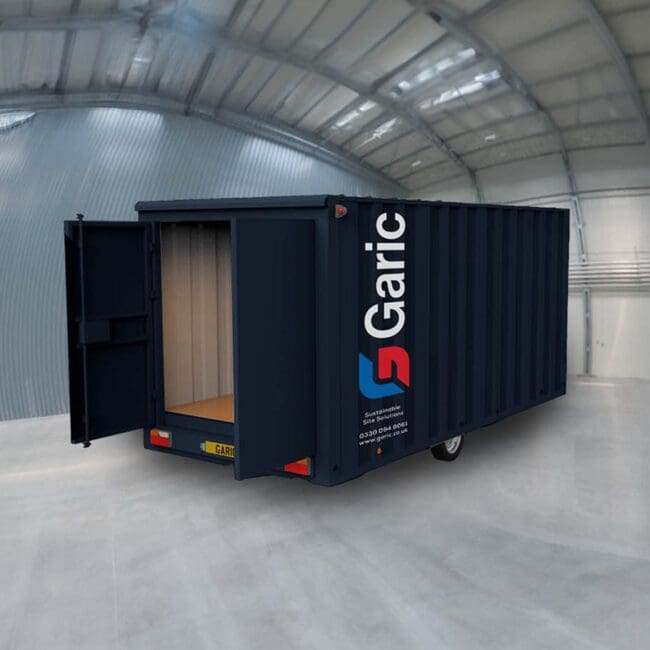 A Mobile Store 12 in dark blue with open doors is positioned inside a large, empty warehouse with a curved roof.
