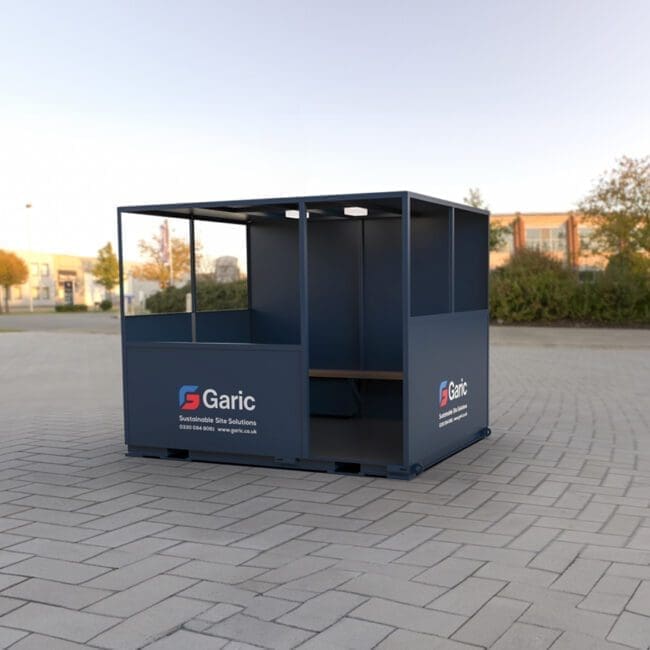 A blue Shelter 10 with benches stands on a paved area, with trees and buildings in the background.