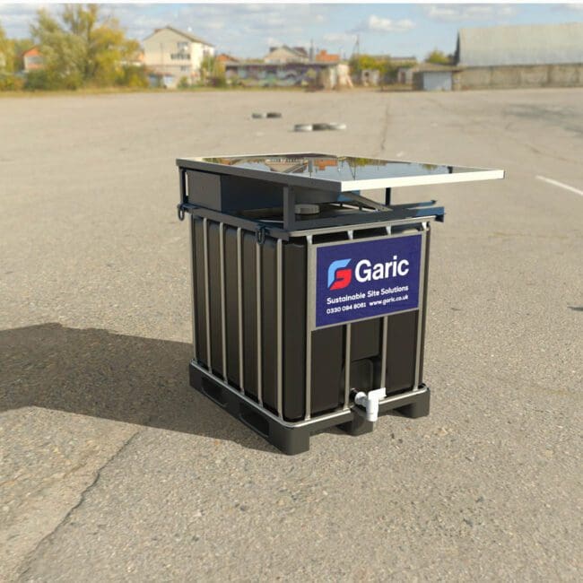 A Solar IBC 1000 sanitation unit, black with a solar panel, stands alone on an empty paved lot beneath a blue sky.