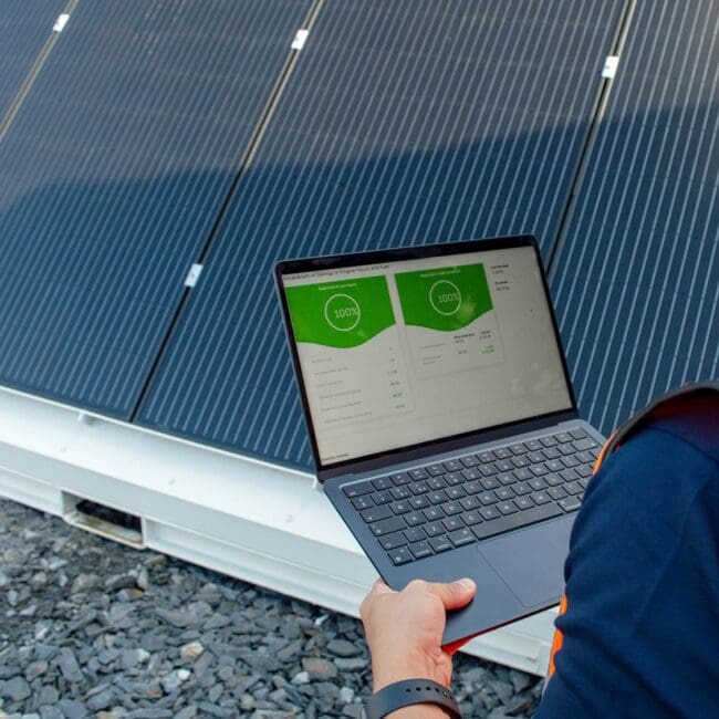 A person stands in front of solar panels holding a laptop that displays energy data, showcasing the Welfare Van Eco+.