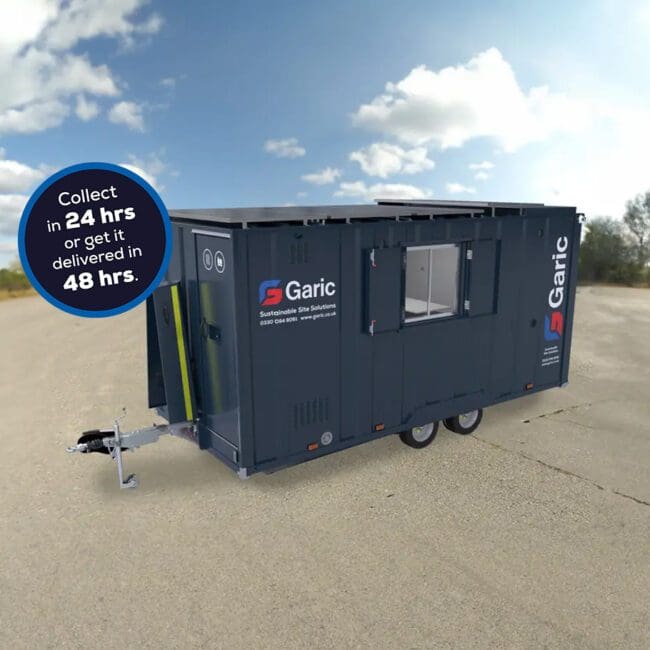 A dark blue Armadillo 18 Eco+ portable unit on wheels in an empty outdoor area, displaying a sign about collection and delivery times.