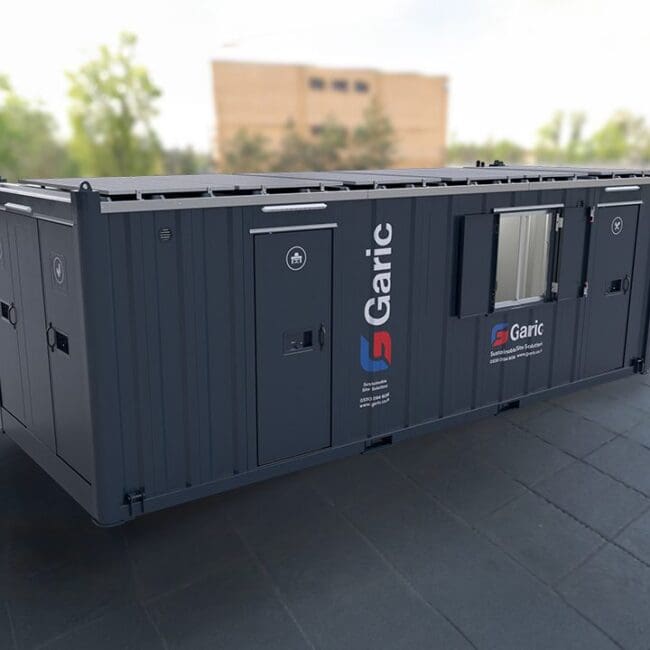 Dark gray portable storage unit with Garic branding, set outdoors on a paved surface, trees in background.