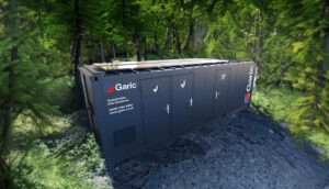 A portable restroom unit by Garic is placed in a forest with sunlight filtering through the trees.