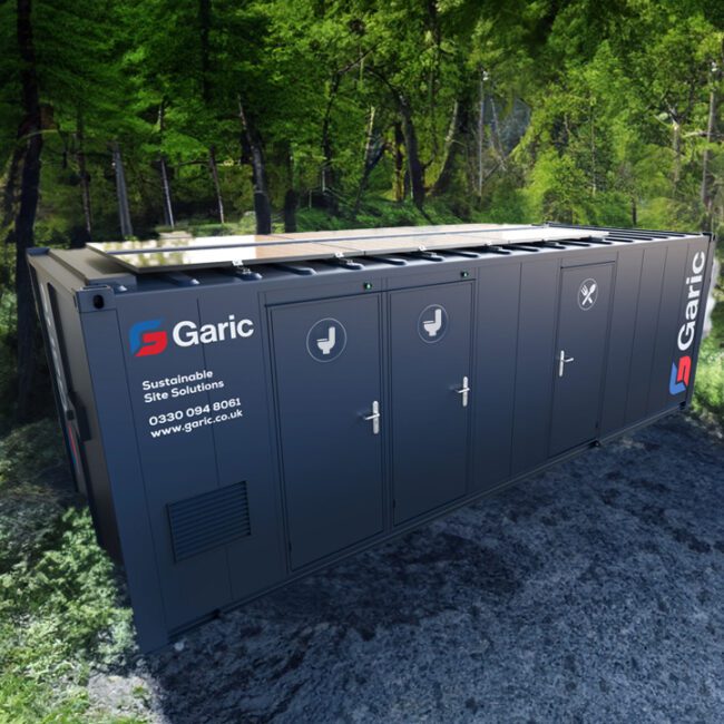 A portable restroom unit by Garic is placed in a forest with sunlight filtering through the trees.