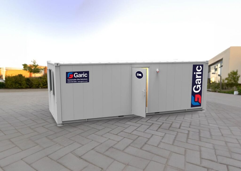 A white portable cabin with Garic logos, placed on a paved outdoor area with its door open.