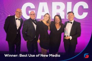 Five people in formal wear smile on stage with an award; text reads Winner: Best Use of New Media.