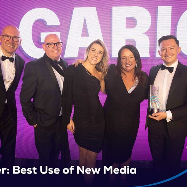 Five people in formal wear smile on stage with an award; text reads Winner: Best Use of New Media.